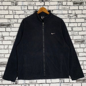 Puede incluir: Chaqueta negra de forro polar con cremallera y un logotipo blanco de Nike en forma de swoosh en el pecho.