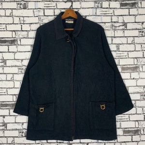 Puede incluir: Una chaqueta negra de manga larga con cierre de cremallera y dos bolsillos. La chaqueta tiene una hebilla de metal dorado en el cuello y dos hebillas de metal dorado en los bolsillos.