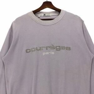 Puede incluir: Una sudadera de manga larga color lavanda con el texto "Courr&egrave;ges Paris" bordado en plata en la parte delantera.