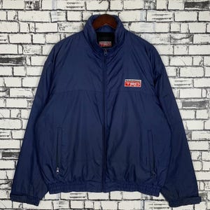 May include: A navy blue zip-up jacket with a "Racing Development" logo and "TRD" text in red and white. The jacket has a zipper closure and two pockets.