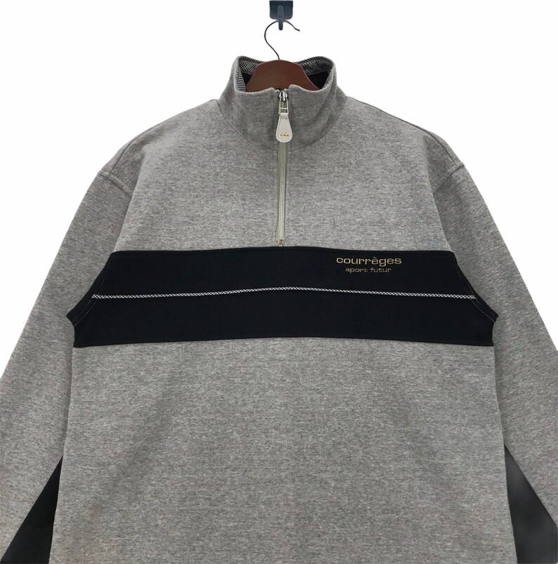 May include: Gray and black long-sleeve sweatshirt with a zipper and a gold logo that reads "Courr&egrave;ges sport futur".