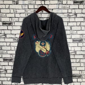 Puede incluir: Una sudadera con capucha gris oscuro con un gr&aacute;fico de avi&oacute;n de estilo vintage en la espalda. El gr&aacute;fico incluye el texto "Air Force 9".