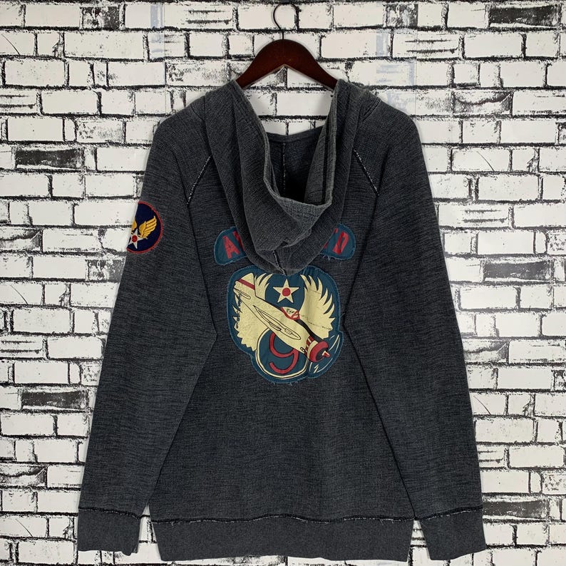 Puede incluir: Una sudadera con capucha gris oscuro con un gr&aacute;fico de avi&oacute;n de estilo vintage en la espalda. El gr&aacute;fico incluye el texto "Air Force 9".