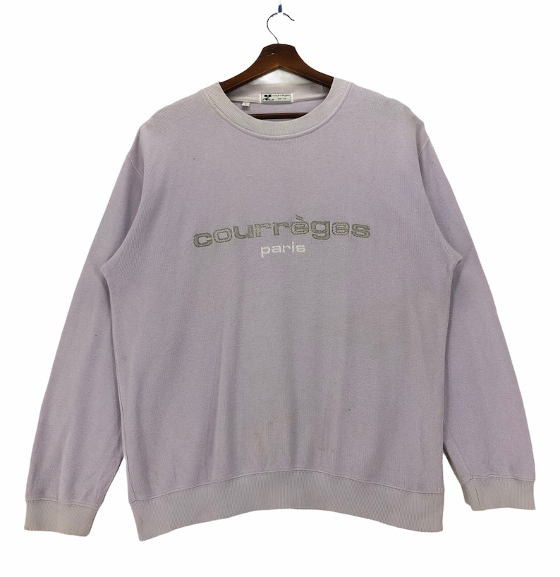 Puede incluir: Una sudadera de color lavanda con el texto "courr&egrave;ges paris" bordado en la parte delantera en color plateado.