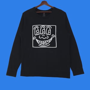 May include: Black long-sleeve sweatshirt with a white graphic of a smiling face with three eyes inside a square.