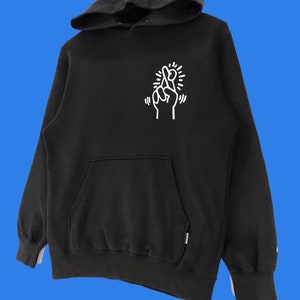 Puede incluir: Sudadera con capucha negra con un gr&aacute;fico blanco de dedos cruzados y un sol en la parte delantera.