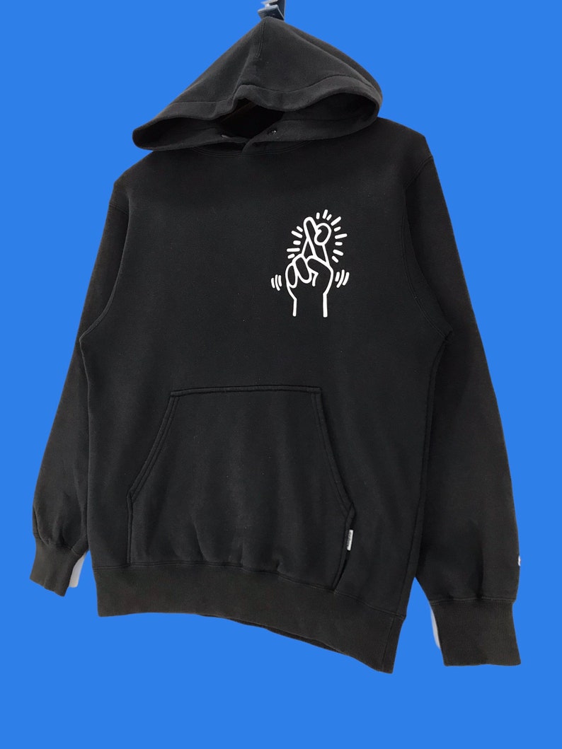 Puede incluir: Sudadera con capucha negra con un gr&aacute;fico blanco de dedos cruzados y un sol en la parte delantera.