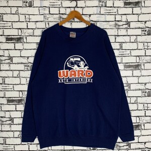 Puede incluir: Una sudadera azul marino con un gráfico de coche vintage y el texto "WARD AUTO INTERIORS" en naranja y blanco.