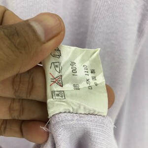 Puede incluir: Una etiqueta blanca con texto negro que dice "100%" y "D-TK-110". La etiqueta tambi&eacute;n tiene un s&iacute;mbolo que indica que la prenda debe lavarse a 40 grados Celsius y un s&iacute;mbolo que indica que la prenda no debe plancharse.