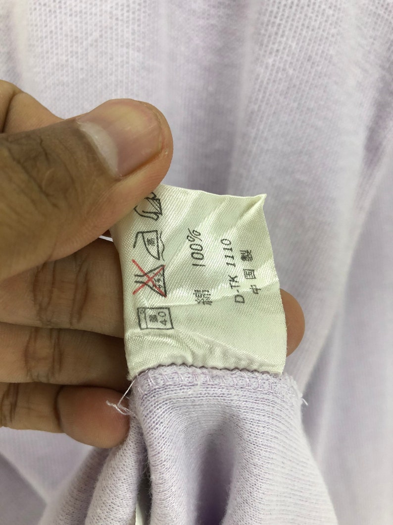 Puede incluir: Una etiqueta blanca con texto negro que dice "100%" y "D-TK-110". La etiqueta tambi&eacute;n tiene un s&iacute;mbolo que indica que la prenda debe lavarse a 40 grados Celsius y un s&iacute;mbolo que indica que la prenda no debe plancharse.