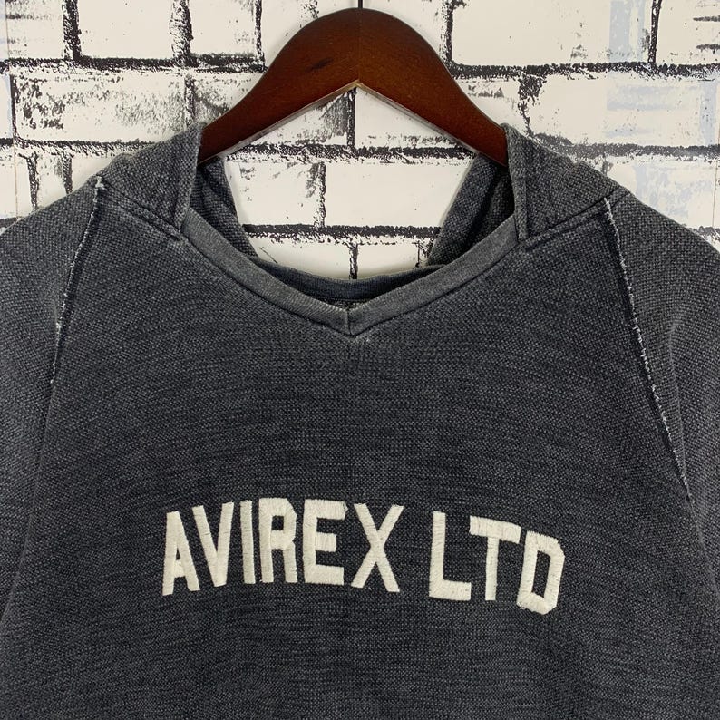 Puede incluir: Una sudadera con capucha negra con el texto "AVIREX LTD" en letras blancas.