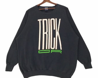 Peut inclure: Sweat-shirt noir avec un imprimé blanc "TRICK OR" sur le devant. Le texte est dans une police de caractères audacieuse et stylisée avec des accents verts.