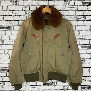 Könnte beinhalten: Eine grüne Bomberjacke mit einem braunen Kunstfellkragen und Ledereinsätzen. Die Jacke hat einen Reißverschluss und zwei Taschen auf der Vorderseite.