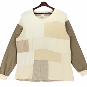 May include: A long-sleeved patchwork shirt in brown, beige and white. The shirt has a crew neck and a relaxed fit.