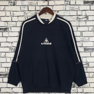 Puede incluir: Una sudadera azul marino con rayas blancas en las mangas y un logotipo bordado en blanco que dice "le coq sportif" con un gallo dentro de un tri&aacute;ngulo.