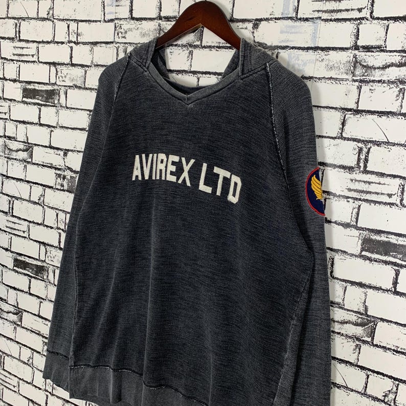 Puede incluir: Una sudadera con capucha negra con un aspecto descolorido. La sudadera tiene el texto "AVIREX LTD" en letras blancas en la parte delantera y un peque&ntilde;o parche amarillo y negro en la manga izquierda.