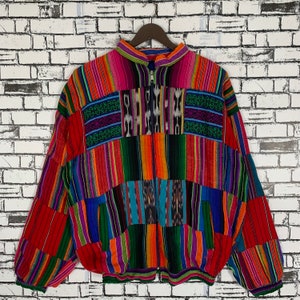 Puede incluir: Una chaqueta colorida, a rayas y con estampado, con cierre de cremallera. La chaqueta está hecha de tejido tejido y tiene un diseño de patchwork.