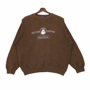 Peut inclure: Un sweat-shirt marron avec un motif blanc représentant un Shetland Sheepdog. Le motif comprend le texte "Shetland Sheepdog" et "Sheltie".