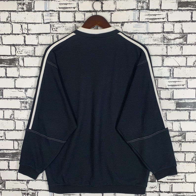 Puede incluir: Una sudadera de manga larga azul oscuro con ribetes blancos alrededor del cuello y las mangas. La sudadera tiene una textura acanalada.