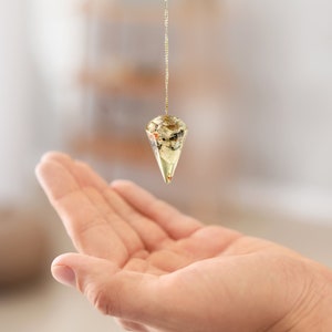 May include: A gold chain with a clear crystal pendulum hanging from it. The pendulum is shaped like a cone and has a variety of small, colourful inclusions inside.