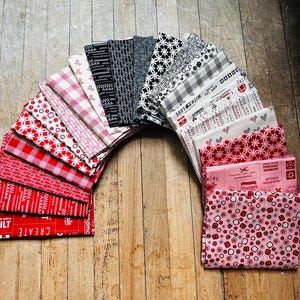 May include: A collection of 18 fabric squares in a rainbow pattern of red, white, and black. The fabric squares are arranged in a semi-circle with the red and white squares on the outside and the black squares on the inside. The fabric squares have various patterns, including polka dots, stripes, and floral designs.