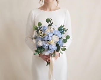 May include: A floral bouquet featuring light blue and white roses, hydrangeas, and green eucalyptus leaves. The arrangement is tied with a long, cream-colored satin ribbon, creating a rounded cluster of artificial flowers and foliage.