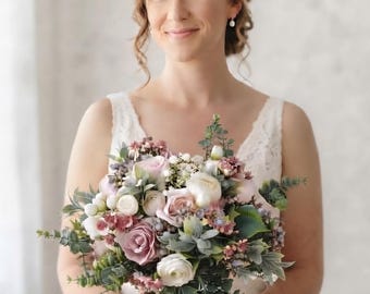 Pode incluir: Um buquê de flores com rosas em tons de rosa seco e branco, pequenas bagas brancas e folhas de eucalipto verdes, atado com uma fita de cor creme. O arranjo inclui várias folhagens texturizadas e flores em tons suaves.