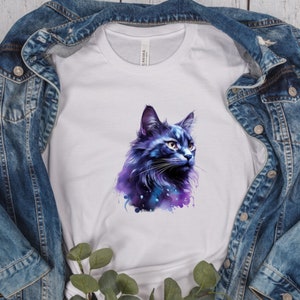 May include: White t-shirt featuring a watercolor illustration of a blue and purple cat. The cat's fur has a galaxy-like design. The shirt is displayed on a denim jacket.
