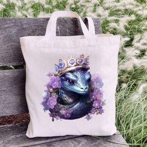 May include: A white tote bag featuring a blue dragon wearing a jeweled crown and surrounded by purple flowers. The dragon has detailed scales and purple eyes. The bag has two white handles.