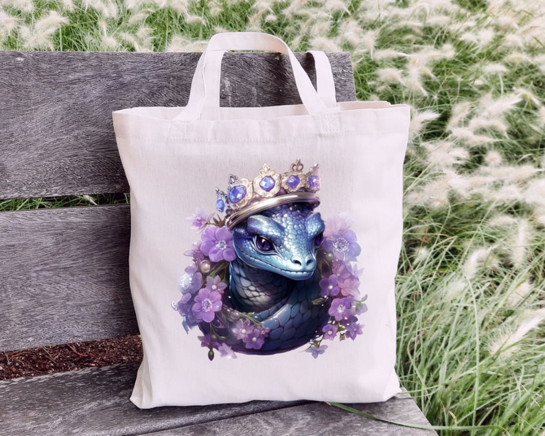May include: A white tote bag featuring a blue dragon wearing a jeweled crown and surrounded by purple flowers. The dragon has detailed scales and purple eyes. The bag has two white handles.