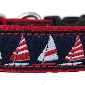 Può includere: Un collare per cani blu navy con bordo rosso e fibbia in plastica nera. Il collare presenta un motivo ripetuto di barche a vela bianche e rosse, creando un tema nautico. Il collare è realizzato in tessuto resistente.