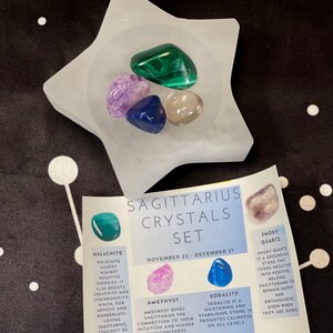 May include: A set of crystals for the zodiac sign Sagittarius, November 22 - December 21. The set includes amethyst, sodalite, smoky quartz, and malachite crystals in a white star-shaped dish. The crystals are described with their properties and how they benefit Sagittarius.