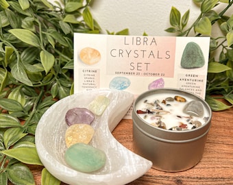 May include: A Libra crystal set with a white selenite moon shaped dish, a candle with crystals and herbs, and four crystals: citrine, amethyst, green aventurine, and clear quartz. The card reads "Libra Crystals Set September 23 - October 22".