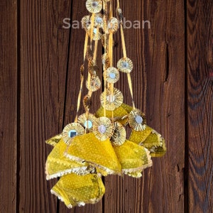 May include: A yellow fabric hanging decoration with multiple layers and small round mirrors. The decoration is hanging from a wooden surface.
