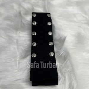 May include: Black fabric headband with silver metal studs. The headband is folded in half and the text "Safa Turban" is visible.