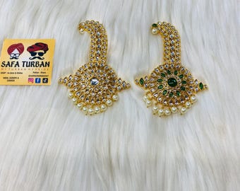 以下が含まれることがあります： 真珠と宝石のアクセントが付いた、金色のターバン装飾が2つ。1つの装飾は白い宝石、もう1つは緑色の宝石が特徴です。
