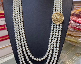 May include: A four-strand pearl necklace with a gold and white round pendant. The pendant has a decorative design with small white stones.