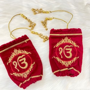 Puede incluir: Dos bolsas de terciopelo rojo con bordados dorados y cordón dorado. Cada bolsa presenta un diseño bordado en oro y el símbolo "ੴ". Las bolsas están adornadas con borlas doradas.
