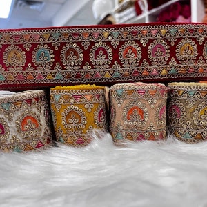 May include: Five spools of colourful embroidered trim with gold accents. The trim features a repeating pattern of small floral designs.