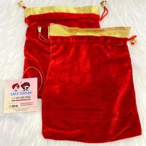 Può includere: Due sacchetti rossi in velluto con coulisse, finiture dorate e piccoli accenti di campanelle dorate. Le borse hanno una consistenza morbida e soffice e sono probabilmente utilizzate per riporre oggetti o come regalo.