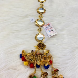 May include: Gold chain with round mirrors and colorful tassels. The chain has six round mirrors with gold frames and a beaded design. The tassels are made of gold fabric and have colorful pom-poms.