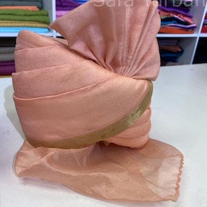 May include: A peach-coloured turban with a gold trim. The turban is folded and arranged in a traditional style.