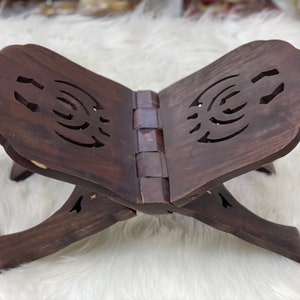 May include: A dark brown wooden book stand with intricate cutouts. The stand is folded and has a hinged design.