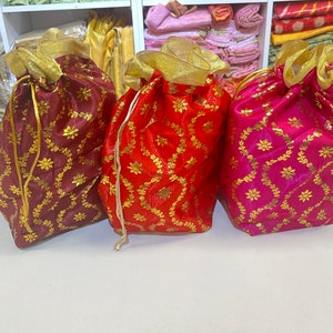 May include: Three decorative drawstring bags made of satin fabric with gold embroidery. The bags are burgundy, red, and pink.