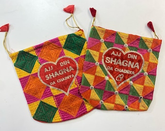 Può includere: Due sacchetti di stoffa rossa con ricami dorati e argentati. I sacchetti sono decorati con un motivo geometrico di quadrati e triangoli in tonalità di rosa, arancio, verde e giallo. Ogni sacchetto ha una toppa rossa a forma di cuore con il testo "AJJ DIN SHAGNA DA CHADEYA" in lettere dorate.