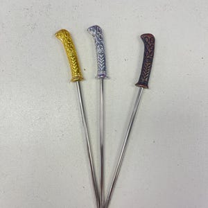 Peut inclure: Trois brochettes en métal avec des poignées décoratives. Les poignées sont dorées, argentées et brunes.