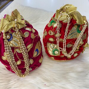 May include: Two velvet drawstring bags. One is a deep magenta, the other is red. Both bags have gold embellishments, beaded tassels, and gold accents. The bags are decorated with embroidered floral and peacock feather designs.