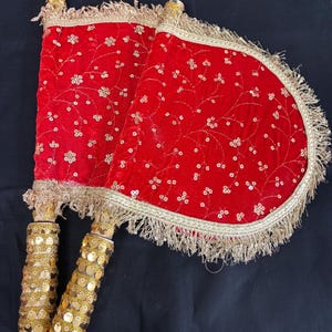 May include: Two red velvet hand fans with gold sequin handles and trim. The fans feature a floral pattern with gold sequins. The cylindrical handles are covered in gold sequins. The fans are set against a black background.