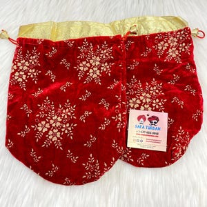 Può includere: Due sacchetti a cordoncino in velluto rosso con bordatura dorata e un motivo floreale dorato. I sacchetti sono su una superficie bianca. Un biglietto da visita con il testo "Safa Turban" è visibile nell'immagine.