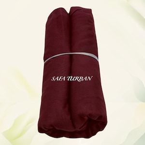 May include: A burgundy fabric turban, rolled up and tied with a gray ribbon. The text "SAFA TURBAN" is printed on the fabric.